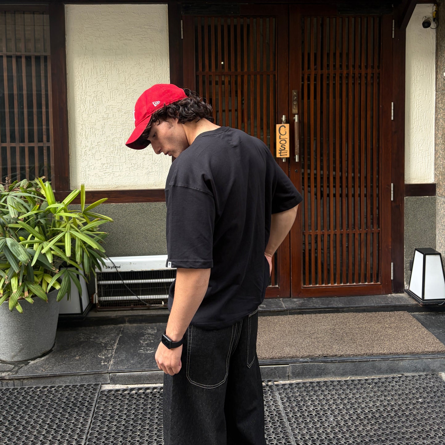 Person wearing a red cap and black shirt standing outside a building with a wooden door.