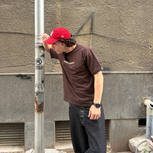 Man wearing a red cap and brown t-shirt leaning against a wall.